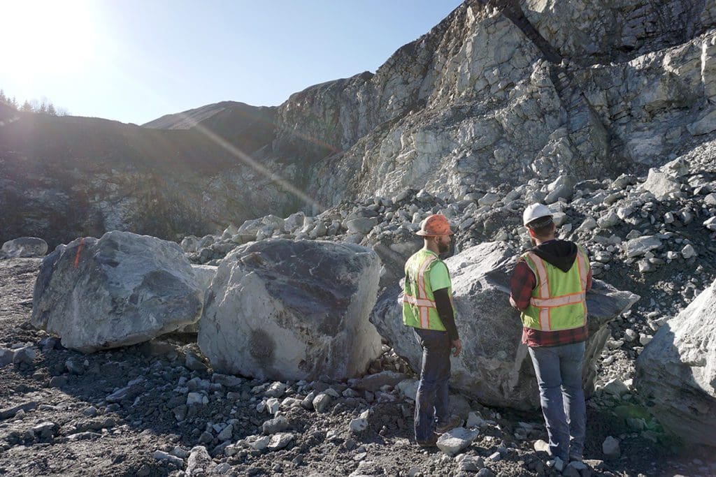 Two men examine an enormous boulder that is almost as tall as they are.