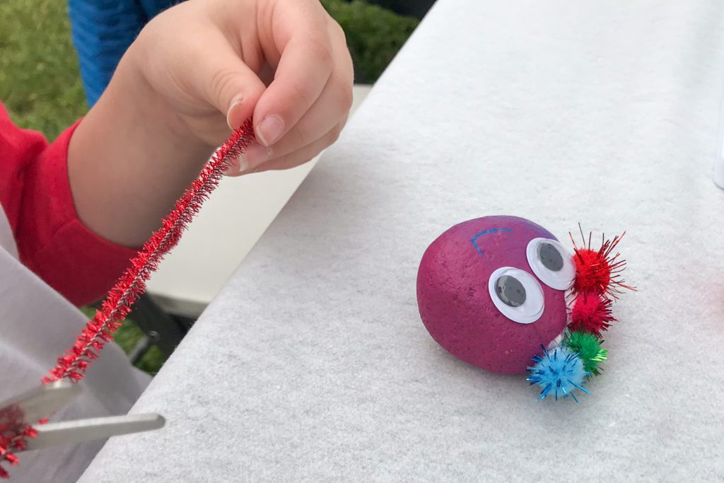 child decorating painted rock with sparkly pipe cleaner