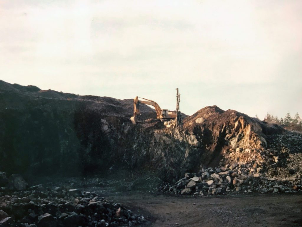 early 1990s photo of loader perched on a rocky hill next to a drill
