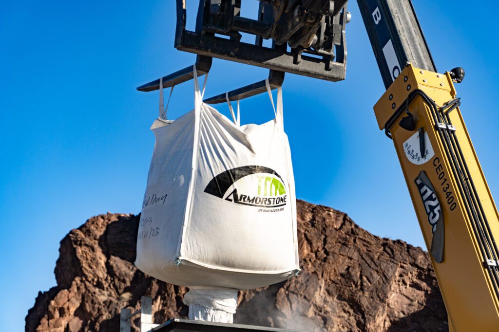 a bag of Armorstone overlay aggregates being hoisted by a forklift with a desert canyon wall in the background