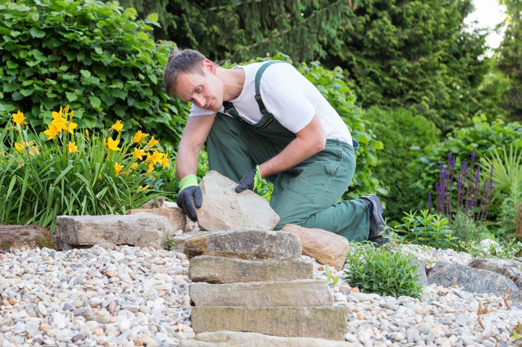 stone worker lays a stone step at the top of a hill
