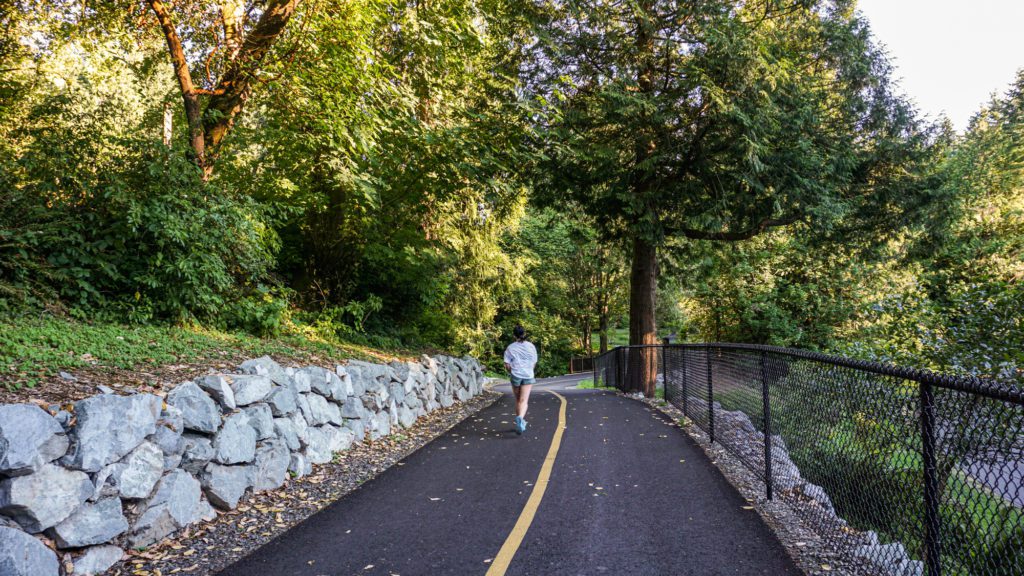 jogger on a road next to rock wall in a forested area