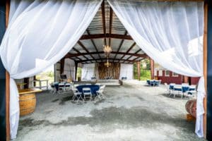 curtain framing the entrance of a gravel event venue filled with tables, chairs, a dance floor, and barrel bar tables