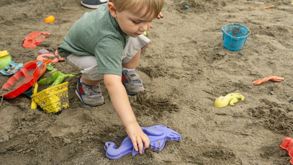 child playing in sandbox with seahorse toy