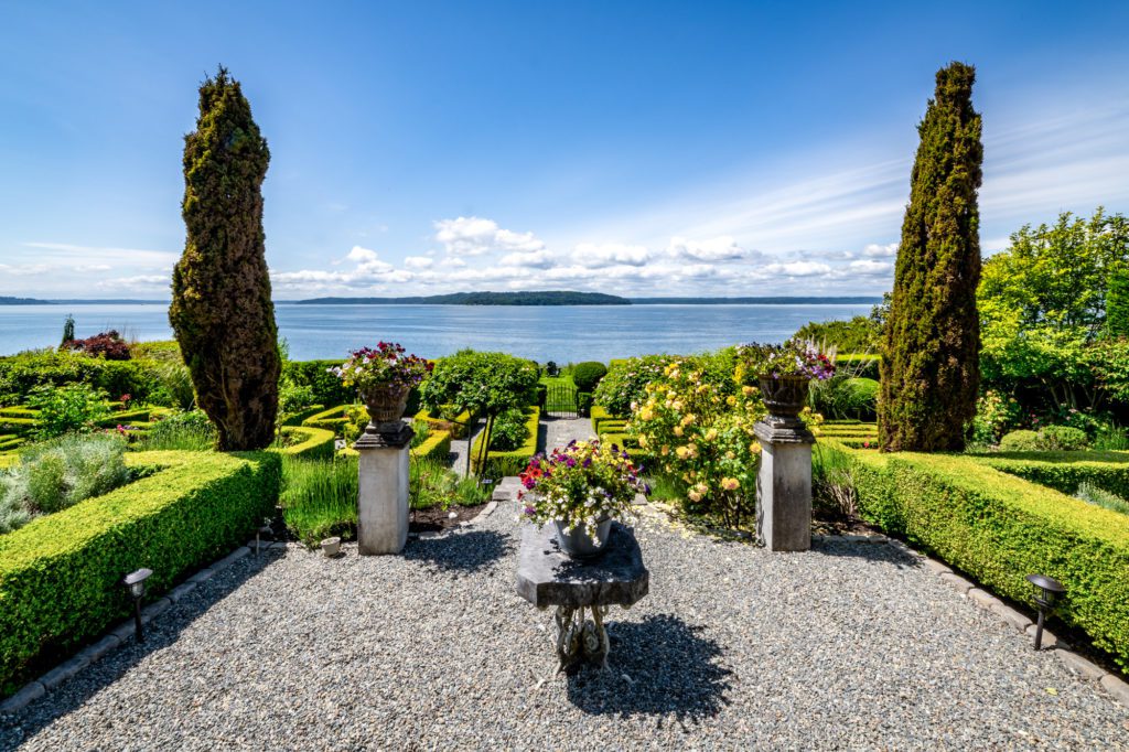 gravel patio with formal boxwood hedges and ocean in distance