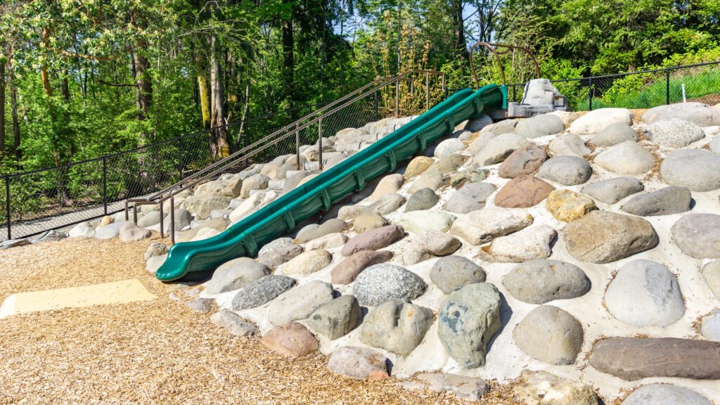 slide in a children's playground surrounded by a sloped area studded with round boulders