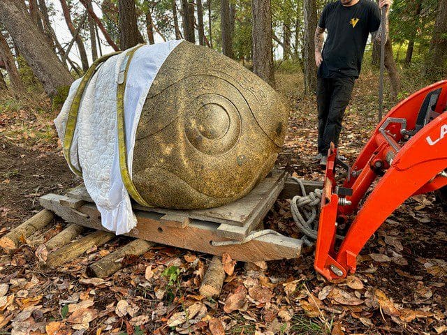 a granite sculpture rests on a pallet next to a small skidsteer