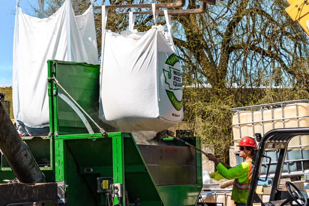 a technician cuts open a Super Sack of pea-sized pebbles that will be added to an epoxy-rubber mix for a synthetic turf field