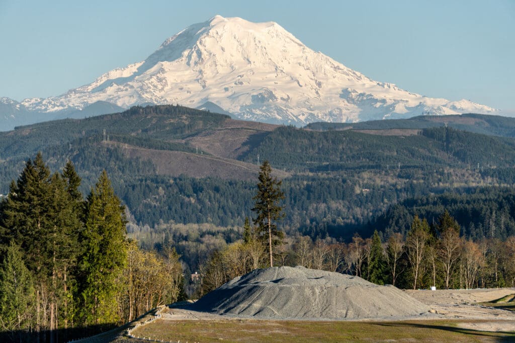 A towering hill of gravel sits in the foreground while Mt. Rainier looms above the foothills in the background.