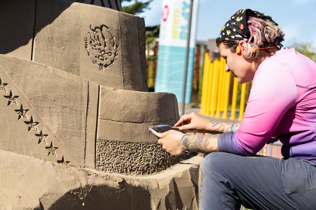 an artist uses a palette knife to carve details into a sand sculpture