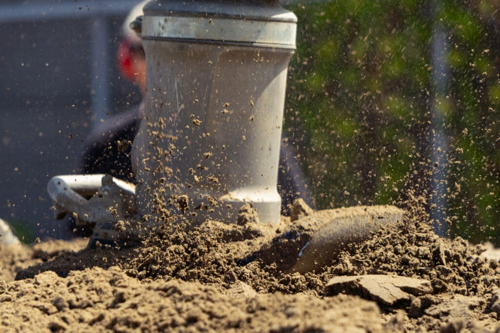 A plate compactor vibrates over the surface of sand.