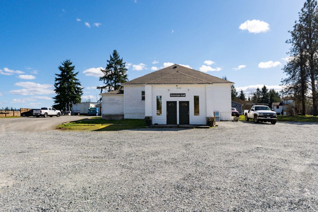 A broad gravel driveway leads to a white country-style building. The scene is sunny.