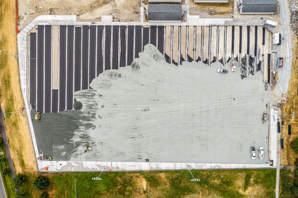 An aerial view shows gravel being pushed over top of a drainage system that extends the length of a field.